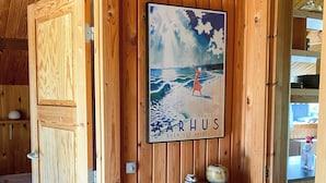 En inredning med trädetaljer, en affisch med en kvinna på en strand, en liten hylla med en vas och en säng med ett blått täcke.