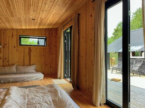 A wooden cabin room with a bed, a window, and a sliding door to an outdoor deck. - Cottage with wilderness bath near beach at Odden (Sjællands Odde)