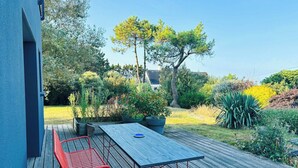 A deck with a table and chairs, surrounded by greenery and trees. - Contemporary haven on the Breton coast (Plouhinec)