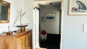 A hallway with a wooden cabinet, a sailboat model, a framed picture, and a door leading to another room. - Contemporary haven on the Breton coast (Plouhinec)