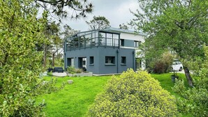 A modern two-story house with a balcony, surrounded by lush greenery and a well-maintained lawn. - Contemporary haven on the Breton coast (Plouhinec)