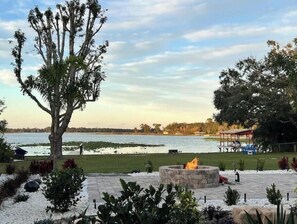 Un patio junto al lago con una chimenea, un árbol grande y un pabellón de fondo.