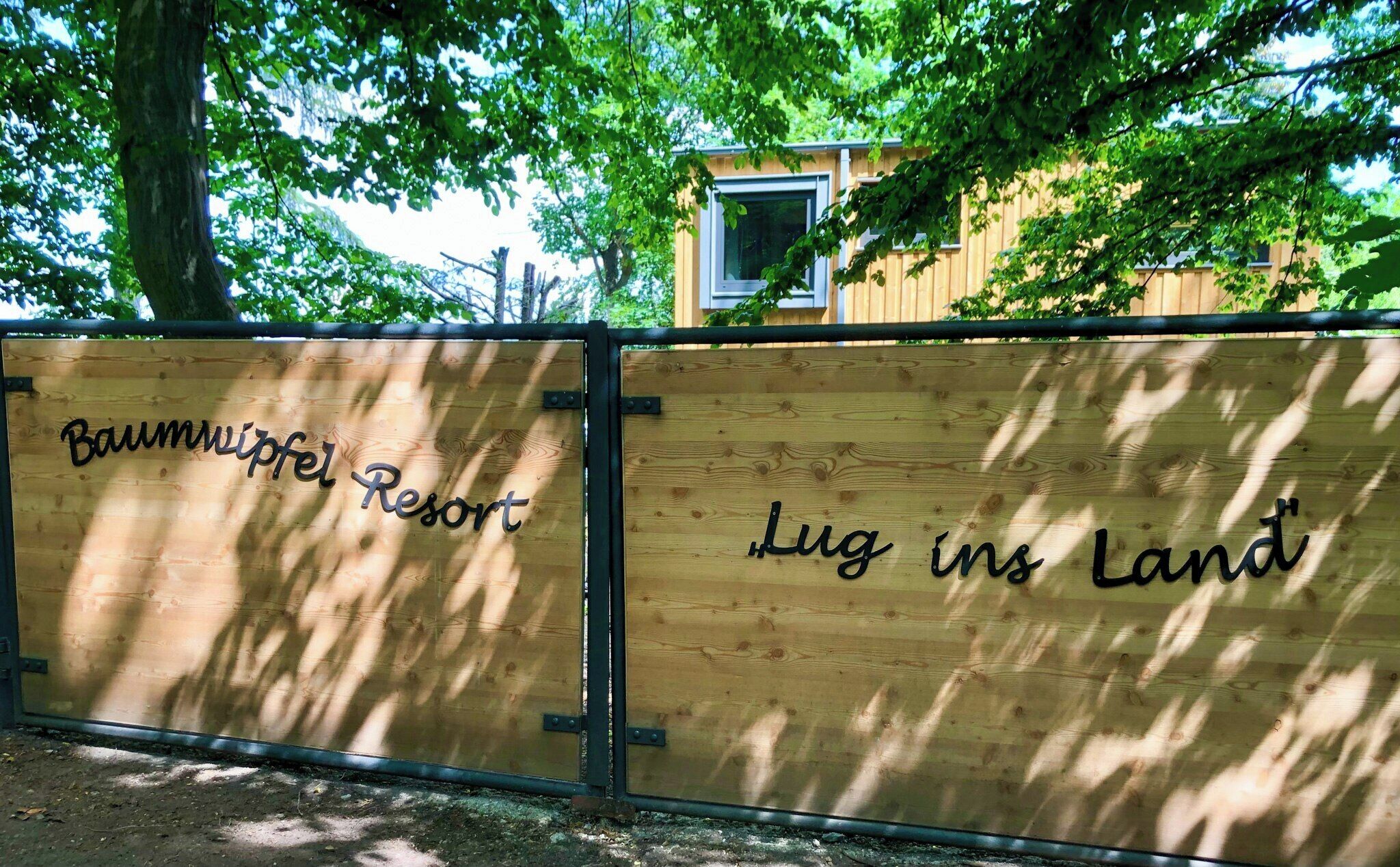 A wooden fence with 'Baumwipfel Resort' and 'Lug ins Land' written on it.