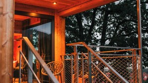 A wooden cabin with a staircase leading to a deck area, a glass door entrance, and a metal railing. - Treetop house near Mount Brocken (Ilsenburg)
