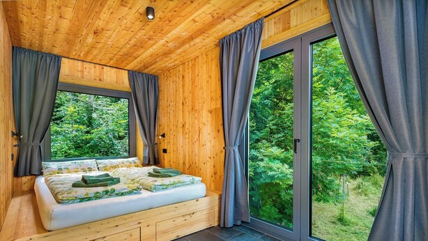 A wooden cabin bedroom with a bed, curtains, and a large window. - Treetop house near Mount Brocken (Ilsenburg)