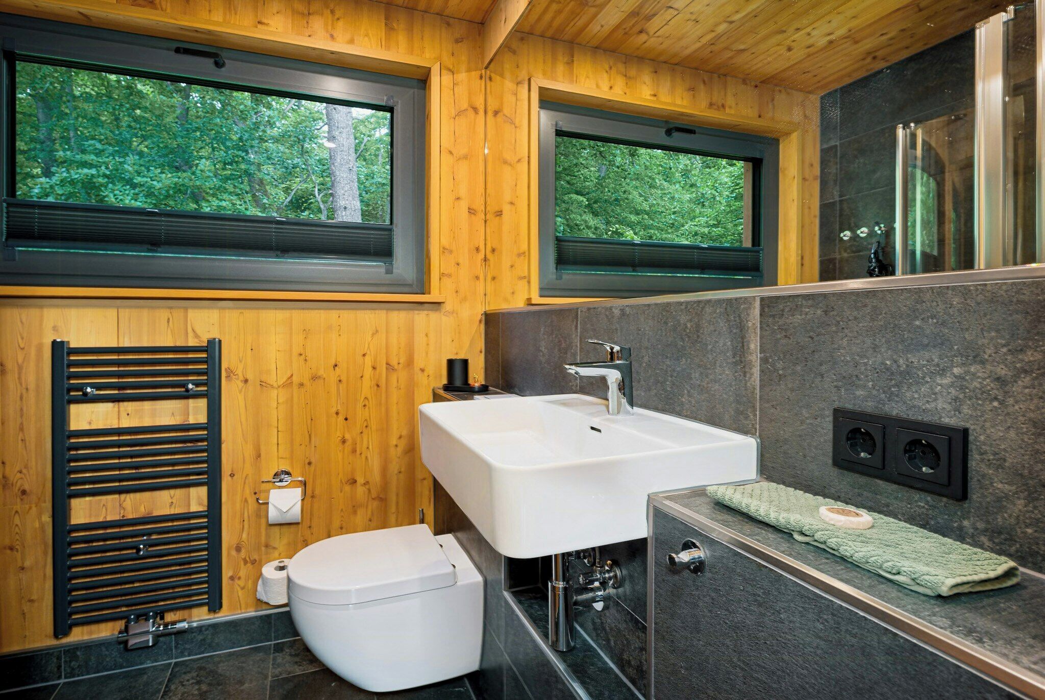 Une salle de bain moderne avec des murs en bois, un lavabo blanc, un porte-serviettes et des toilettes.
