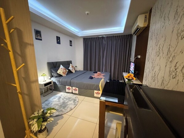 A bedroom with a bed, a desk, a TV, and a plant. - cozy studio unit laguna 2 (Muang Pattaya)