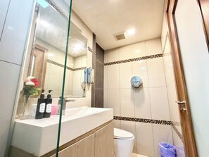 A bathroom with a glass shower enclosure, a white sink with toiletries, and a toilet. - cozy studio unit laguna 2 (Muang Pattaya)