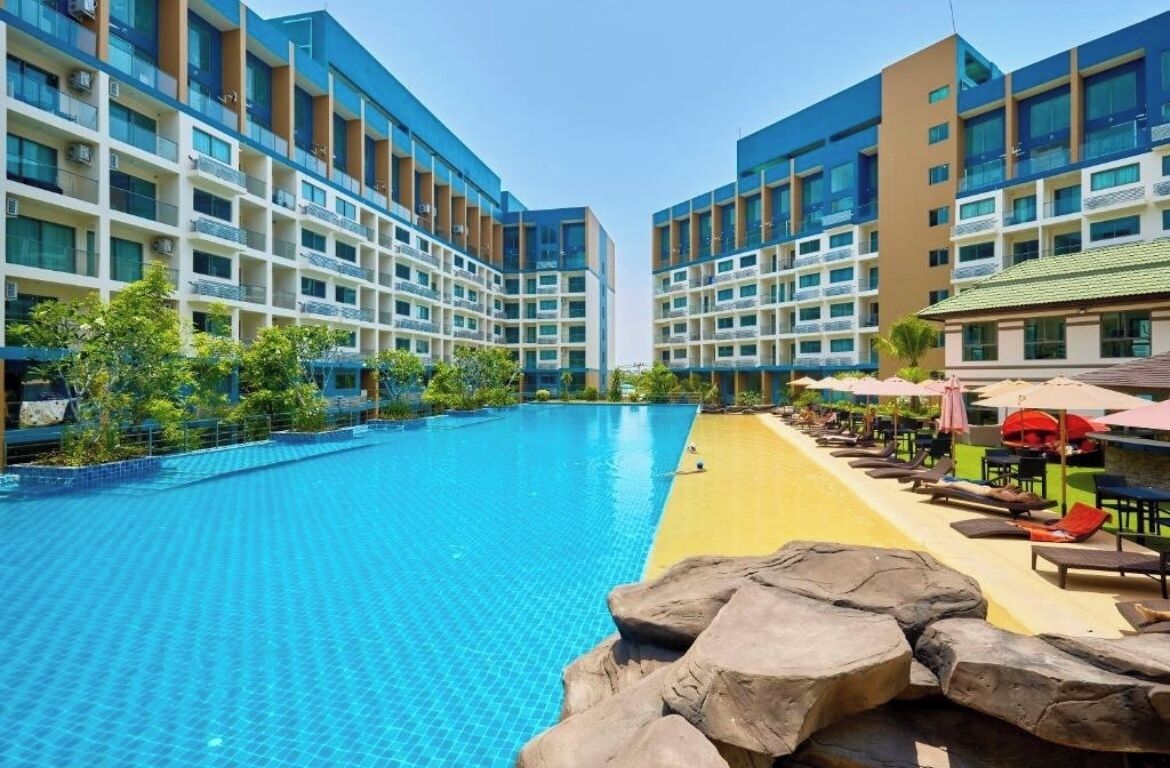 A modern hotel with a central swimming pool, multiple balconies, and outdoor seating areas.
