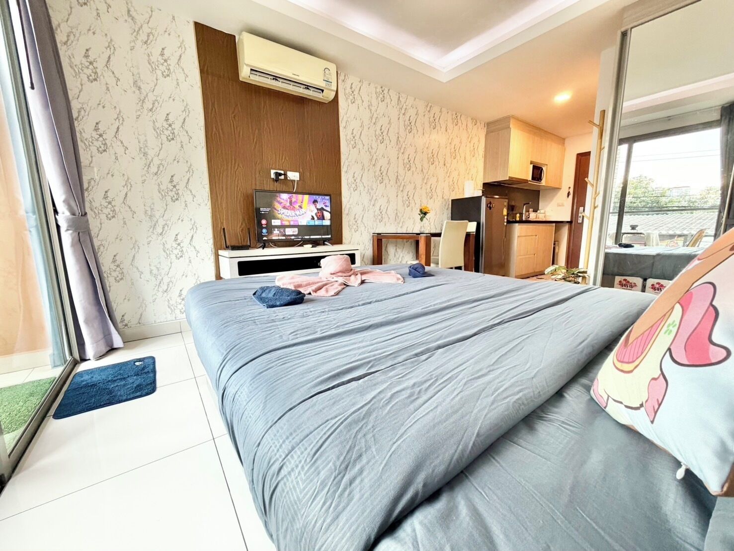 A hotel room with a bed, a TV, a desk, and a kitchenette.