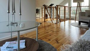 Ein modernes Wohnzimmer mit Glastisch, Holzboden, einem weißen Sofa und einem großen Fenster.