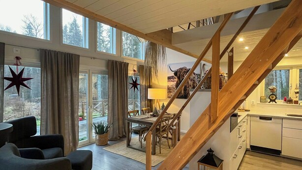 Ein großzügiger Wohnbereich mit einer Holztreppe, einem Esstisch und Blick durch große Fenster.