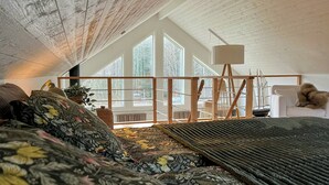Ein Schlafzimmer mit schrägen Wänden, einem Bett mit Blumenbettwäsche, einem Fenster mit Blick auf Bäume und einem Modell eines Segelbootes.