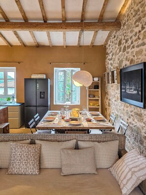 Un comedor con pared de piedra, vigas de madera, un refrigerador negro y una mesa de comedor lista para seis personas.