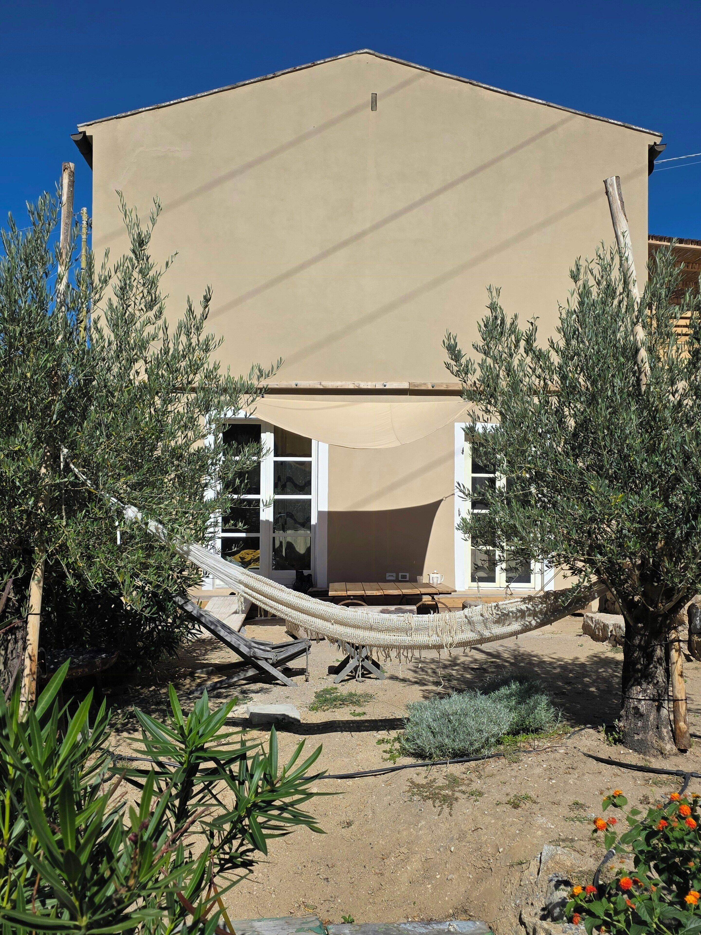 A building with a beige exterior, a hammock, and surrounding greenery.