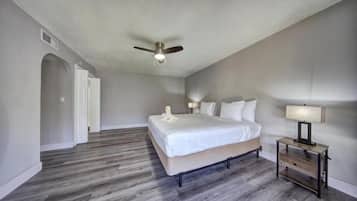 Un dormitorio con cama, ventilador de techo, mesita de noche y puerta que da a otra habitación.