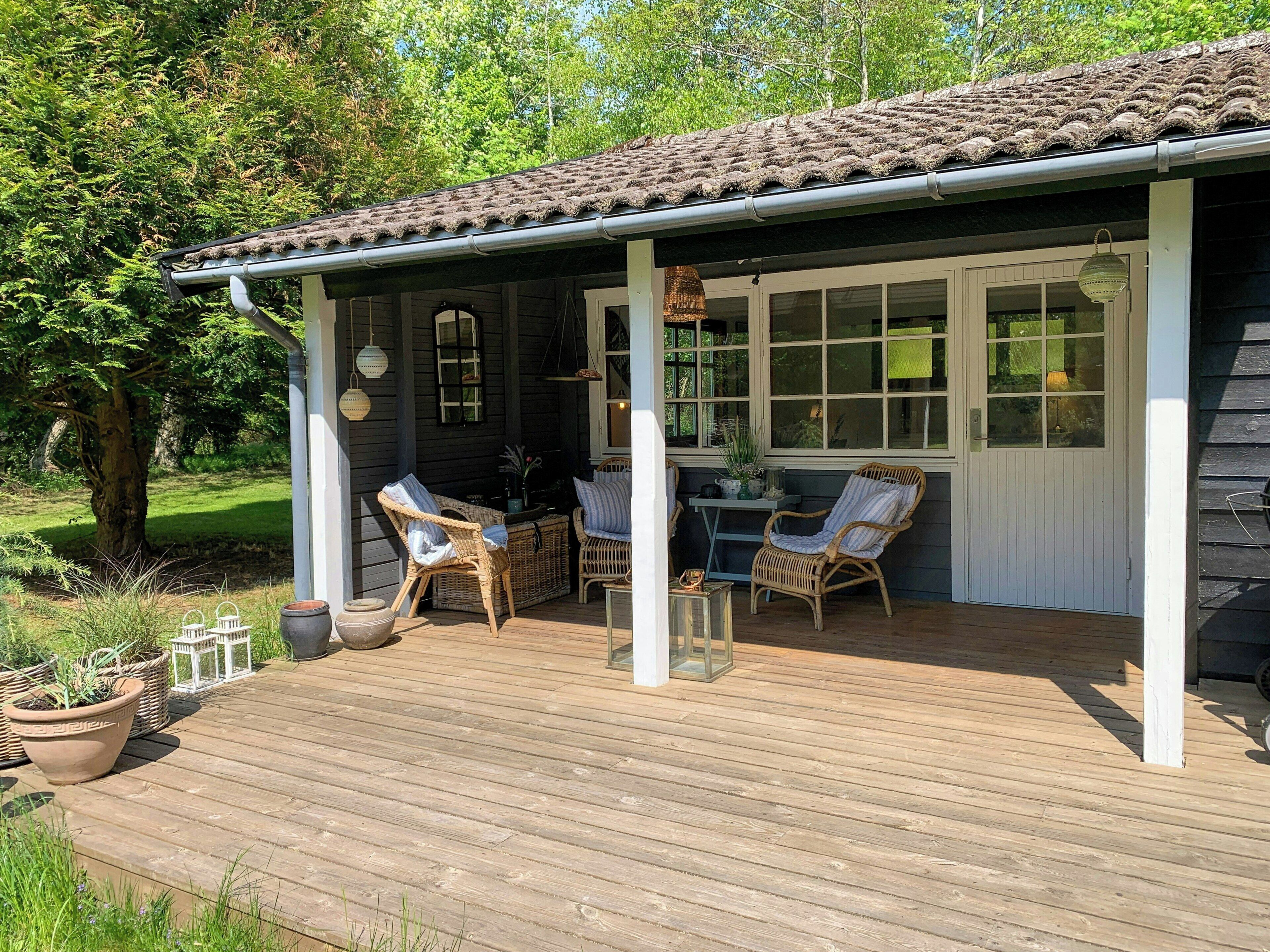 A covered outdoor seating area with wicker furniture, a table, and potted plants.