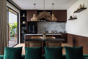 Een moderne keuken met donkerhouten kastjes, een marmeren aanrechtblad en een eethoek met groen gestoffeerde stoelen.