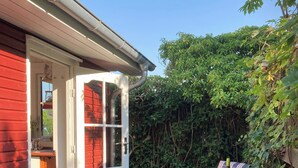 Eine Terrasse mit Tisch und Stühlen, ein rotes Gebäude und eine Tür zu einem Innenbereich.