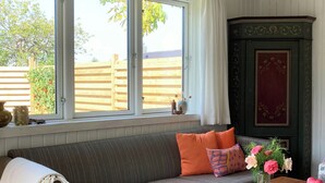 Ein Zimmer mit einer Couch, einem Tisch und einem Fenster mit Blick auf einen Holenzaun.