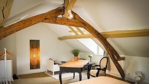 A cozy attic bedroom with exposed wooden beams, a white bed, a small table, a chair, and a potted plant. - Charming house by the Seine in Normandy (Poses)