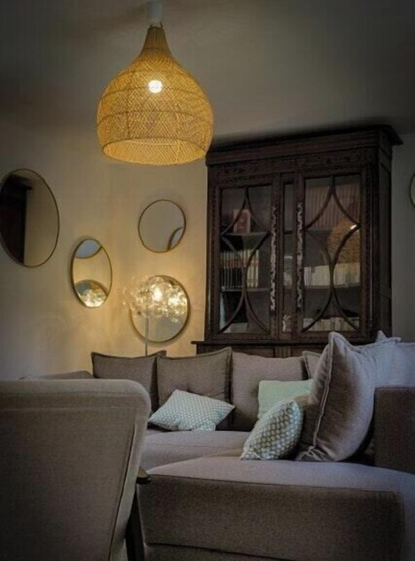 A cozy living room with a sofa, cushions, a hanging light fixture, and a wooden cabinet.