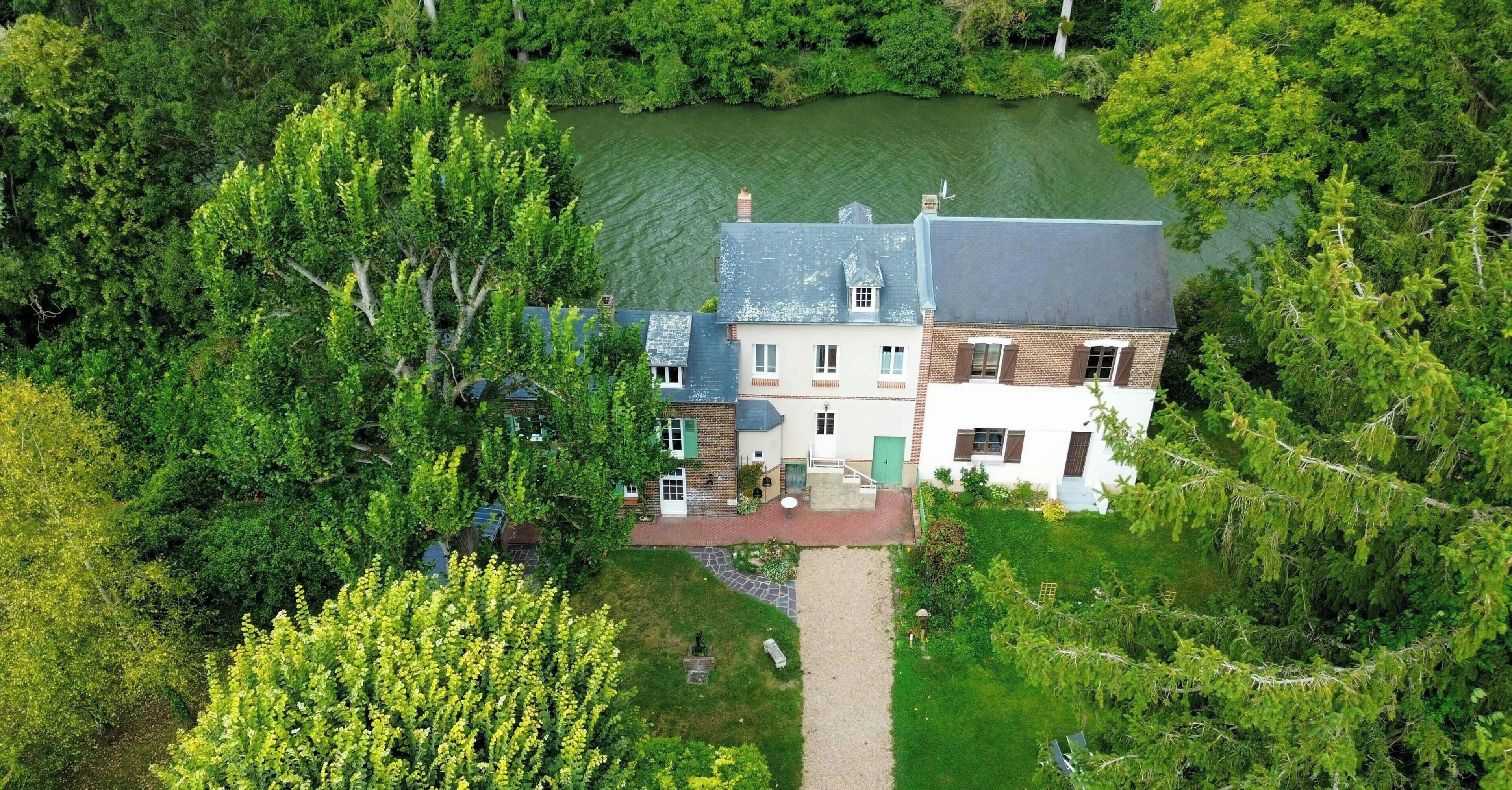 A large house with a pond in front, surrounded by dense trees.