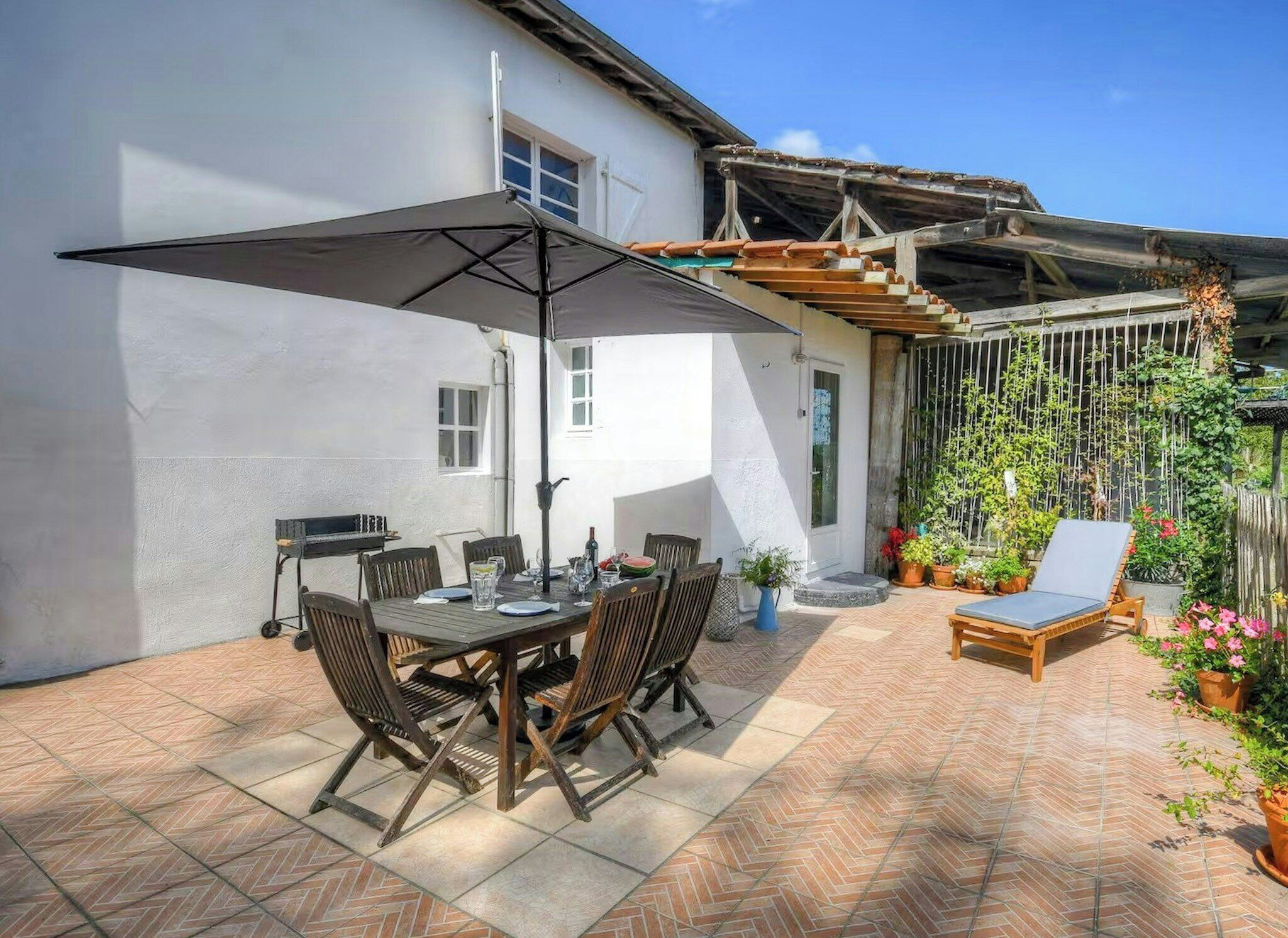 An outdoor patio with a table and chairs, a grill, and a covered seating area with plants.
