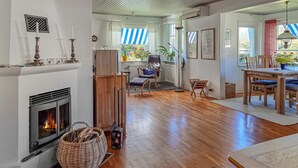 Una sala de estar acogedora con chimenea, suelo de madera, una zona de comedor con mesa y sillas, y vistas al exterior a través de amplios ventanales.