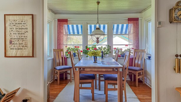 Un comedor con una mesa de madera, sillas, una lámpara de araña y un ventanal con cortinas a rayas.