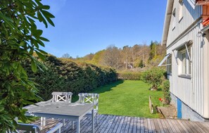 A wooden deck with a table and chairs, a well-maintained lawn, and a building with a corrugated metal exterior. - Stunning home in Billdal with WiFi (Billdal)