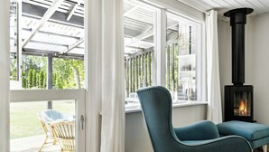 Een kamer met een groot raam, een bank, een rieten stoel en een open haard.