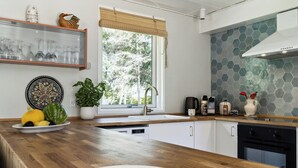 Een keuken met een houten aanrecht, een raam met uitzicht op bomen, een spoelbak en diverse keukenbenodigdheden.