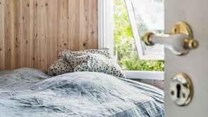 Een slaapkamer met een houten wand, een bed met een gebloemd plaid en een raam met uitzicht op groen.