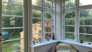 A room with a large bay window, a wicker chair with a white cushion, and a small table with a basket. - Villa from 1917 high above Tisvildeleje (Tisvilde)