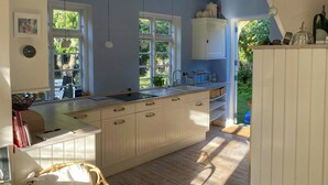 A kitchen with a large island, wooden flooring, and a wicker chair. - Villa from 1917 high above Tisvildeleje (Tisvilde)