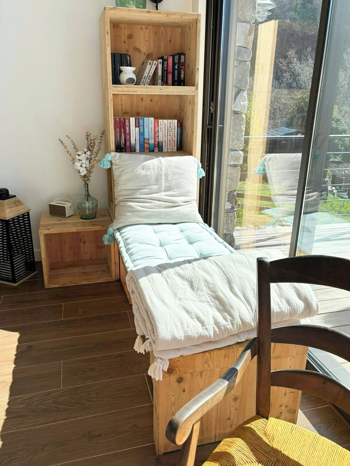 Une pièce chaleureuse avec un lit en bois, une bibliothèque, une petite table sur laquelle est posé un vase, et une chaise.