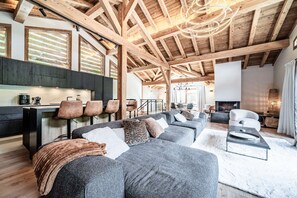 Ampla sala de estar com teto alto, vigas de madeira, cozinha equipada com eletrodomésticos modernos e um aconchegante espaço para sentar.