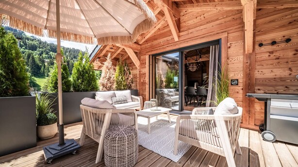 Eine Holzterrasse mit Gartenmöbeln, einem Grill und Blick auf eine bewaldete Landschaft.
