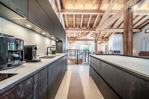 Cozinha com máquina de café expresso moderna, vigas de madeira e vista para uma varanda.