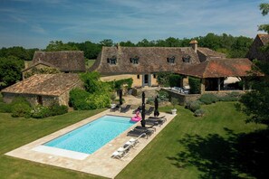 A swimming pool with lounge chairs and umbrellas, surrounded by stone buildings with thatched roofs. - Large 16th century farm estate in Dordogne (Sainte Croix)