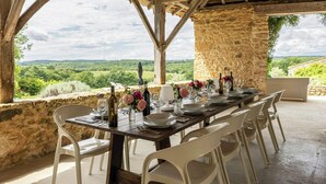 A dining table set for six with white chairs, a stone wall, and a view of the countryside. - Large 16th century farm estate in Dordogne (Sainte Croix)