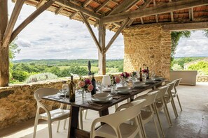 A dining table set for six with white chairs, a stone wall, and a view of the countryside. - Large 16th century farm estate in Dordogne (Sainte Croix)