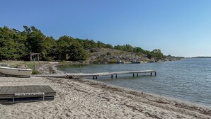 A beach with a wooden pier extending into calm water, surrounded by trees and a small building. - Beautiful home in Nynäshamn with WiFi (Nynäshamn)