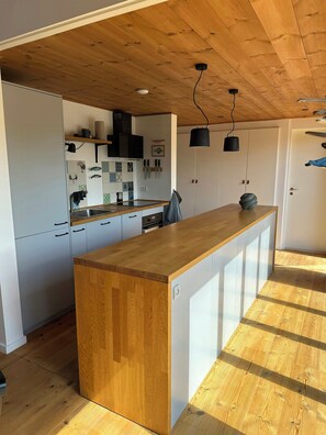 A modern kitchen with wooden cabinets, a central island, and pendant lighting. - Holiday home with hot tub near Ebeltoft (Ebeltoft)