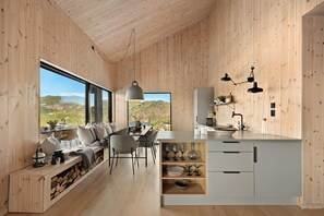 A modern kitchen with wooden walls, a dining area with a view, and a built-in bench with storage. - Cabin overlooking Ryfylke fjord (Høyvik)