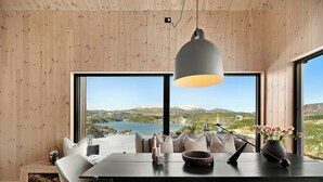 Ein Essbereich mit Holztisch, Stühlen, einer Hängeleuchte und Blick auf einen See und Berge durch große Fenster.