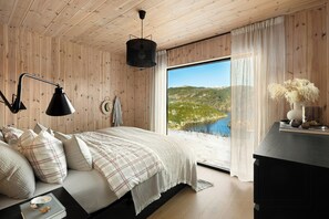 A bedroom with a large bed, a desk, a view of a lake, and wooden walls. - Cabin overlooking Ryfylke fjord (Høyvik)