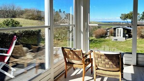 Ett rum med stora fönster, flätade stolar och utsikt över ett hus och ett landskap.