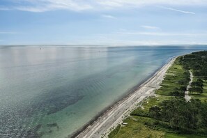 An aerial view of a coastal area with a beach, a road, and greenery. - Big family dream of a summer home (Ebeltoft)
